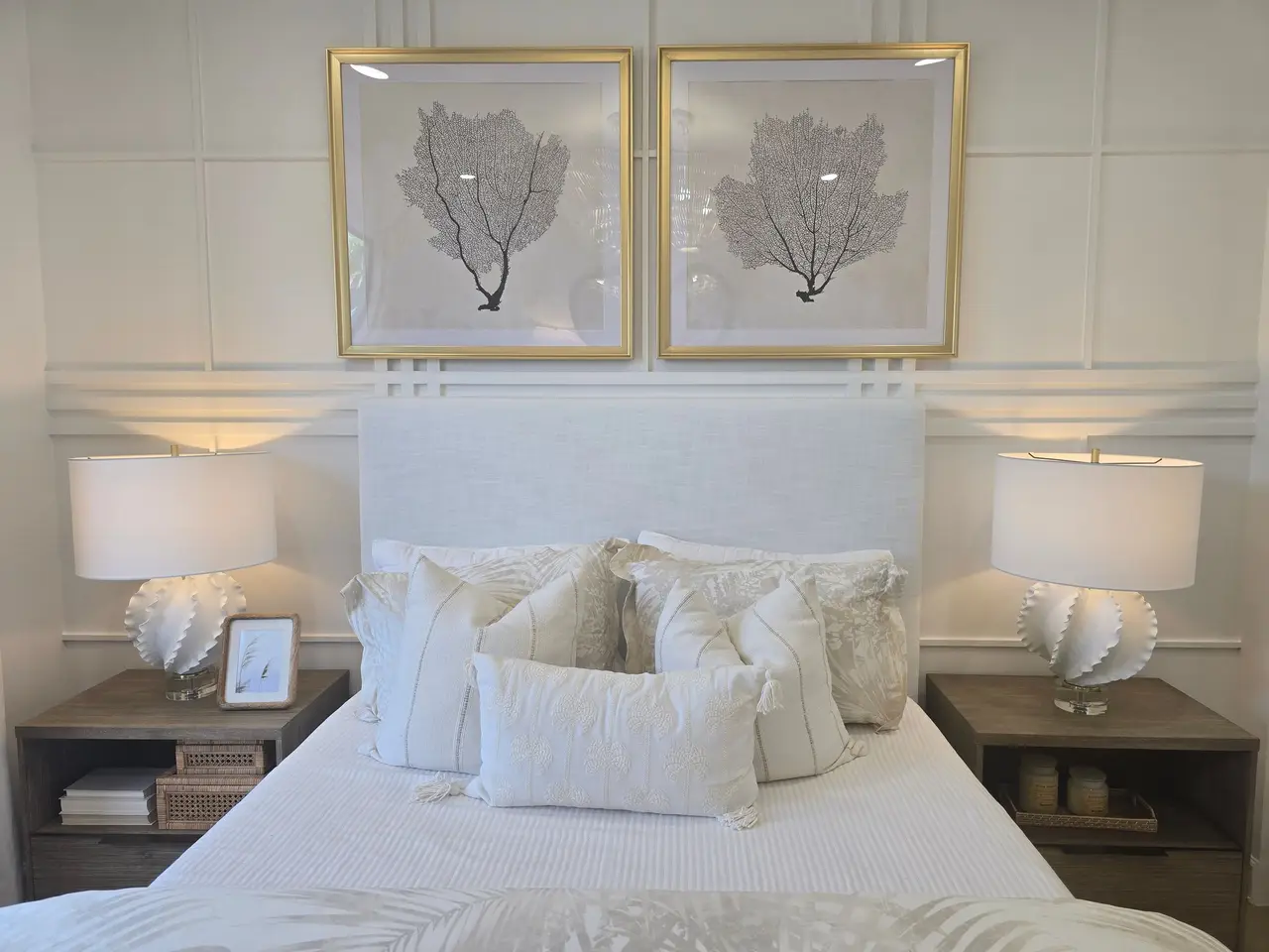 A made bed with crisp white linens beneath two framed sea-fan prints.