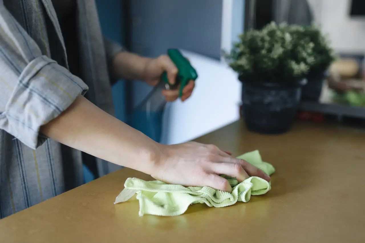 A hand wiping a countertop with a sea-green microfiber cloth.