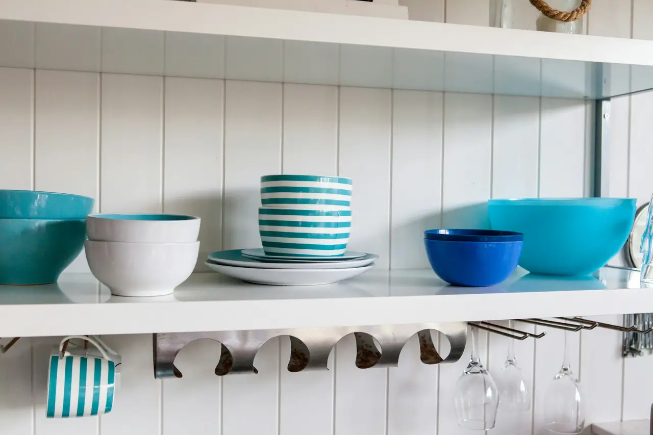 White beadboard shelves stacked with teal and blue bowls in a beach-house kitchen.